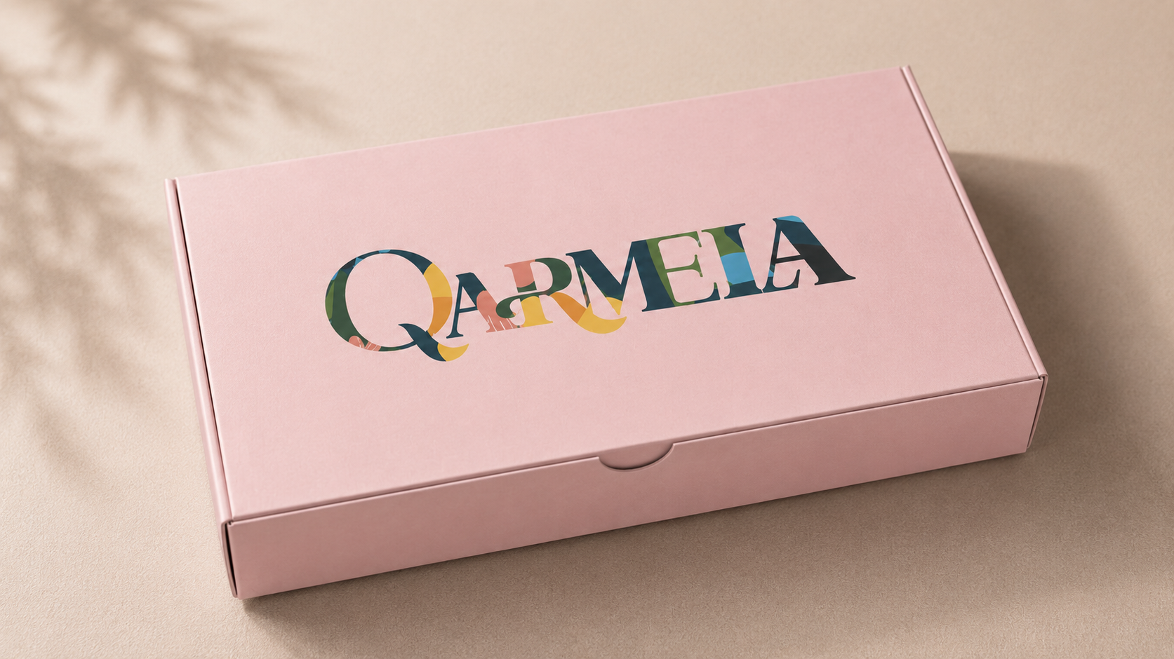 Qarmela — pink gift box packaging with botanical logo and soft shadow on warm beige background