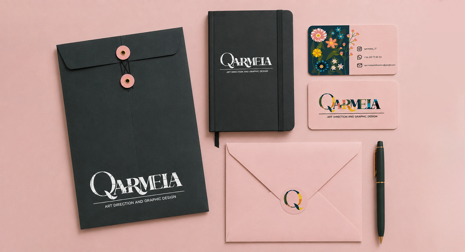 Qarmela — complete stationery suite including dark envelope, notebook, business cards, pink envelope and pen on coral background